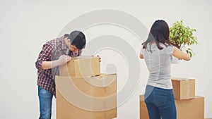 Couple in new flat. Young man is totaly exhausted. He can not carry heavy boxes. Woman is standing, smiling, holding