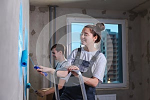 Couple in new home during repair works painting wall together. Happy family holding paint roller painting wall with blue