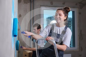 Couple in new home during repair works painting wall together. Happy family holding paint roller painting wall with blue