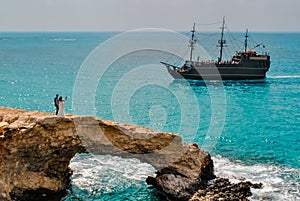 A couple of newlyweds, a bride and groom, stand on the rocky Love Bridge in Cyprus, near Ayia Napa. Against the