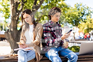 Couple not talking to each other typing on mobile phones sitting in the bench on the street