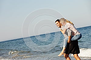 Couple, ocean waves and piggyback on vacation, smile and peace at beach or game by blue sky. People, happy and tropical