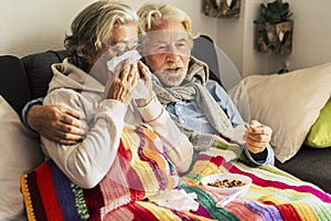 Couple of old aged senior people at home with seasonal winter cold illness disease  sit down on the sof together forever - health