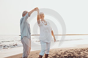 Couple of old mature people dancing together and having fun on the sand at the beach enjoying and living the moment. Portrait of