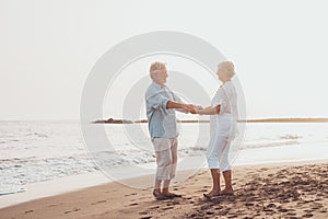 Couple of old mature people dancing together and having fun on the sand at the beach enjoying and living the moment. Portrait of