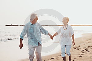 Couple of old mature people walking on the sand together and having fun on the sand of the beach enjoying and living the moment.
