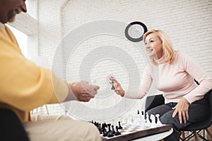 A couple of old people play chess at home. They play with delight and joy.