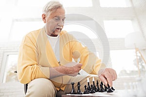 A couple of old people play chess at home. They play with delight and joy.