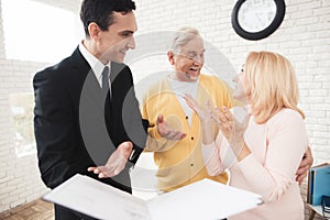 A couple of old people at a reception with a realtor. Joyful old men are standing next to the realtor.