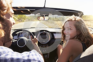 Couple in open top car look at each other, passenger POV