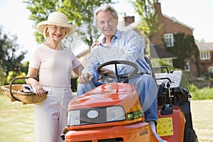 Couple outdoors with tools and lawnmower smiling