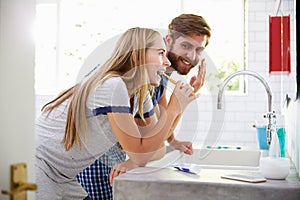 Couple In Pajamas Brushing Teeth And Putting On Moisturizer