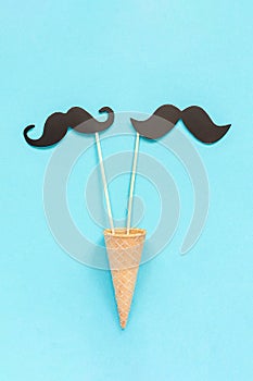 Couple paper mustache props on stick in ice cream waffle cone on blue background. Concept Homosexuality gay love. International