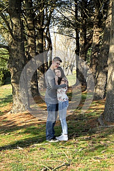 Couple pausing for affection among tall pine trees holding hands.