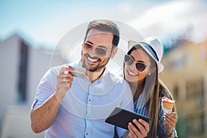 Couple paying on line with credit card and digital tablet on the street