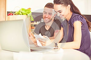 Couple paying their bills with laptop in kitchen at home