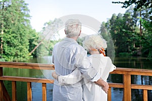 Couple of pensioners hugging each other looking at beautiful lake