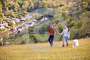 Couple With Pet Golden Retriever Dog Walking Along Path Across Field In Countryside