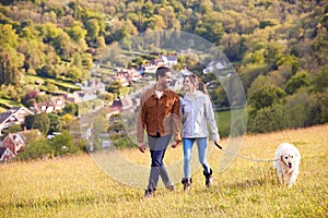 Couple With Pet Golden Retriever Dog Walking Along Path Across Field In Countryside