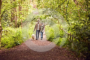 Couple With Pet Golden Retriever Dog Walking Along Path Through Trees In Countryside