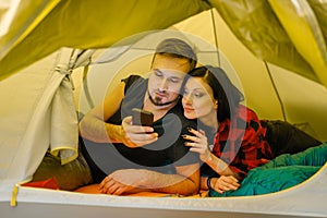 Couple with phone lying in tourist tent