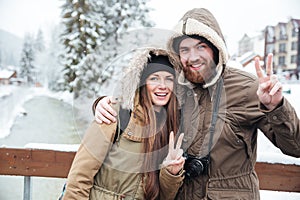 Couple with photo camera showing peace gesture on winter resort