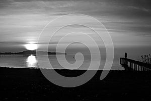 A couple on a pier on the lake at the sunset, with sun coming down behind and island