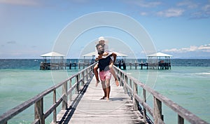 Couple, piggyback and outdoor beach deck on a tropical island with love and water on holiday. Summer vacation, travel