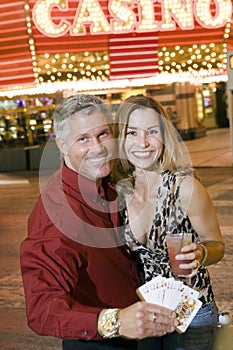 Couple With Playing Cards And Drink Standing Against Casino