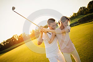 Couple playing golf together at sunset, swinging together to hit the ball with a golf club