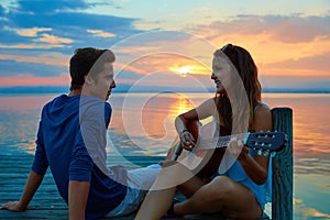 Couple playing guitar in sunset pier at dusk beach