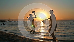 Couple playing tennis on the beach at sunset