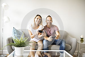 Couple playing video games at home, sitting on sofa