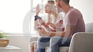 Couple playing video games at home, sitting on sofa