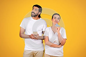 Couple pondering online purchase with a credit card, yellow backdrop