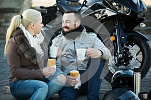 Couple posing near motor bike with sandwitches and coffee