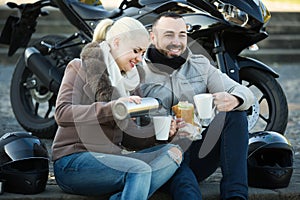 Couple posing near motor bike with sandwitches and coffee