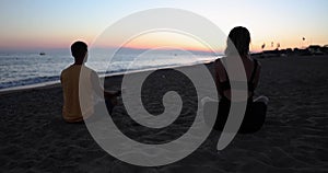 Couple practice yoga and meditate together by sea during sunset