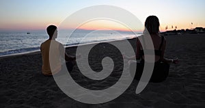 Couple practice yoga and meditate together by sea during sunset