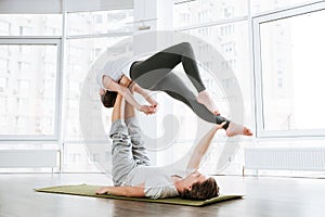 Couple practicing acro yoga on green mat in studio together