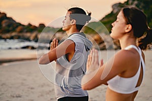 Couple, prayer hands and yoga meditation at beach outdoors for health and wellness. Sunset, pilates fitness and man and