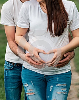 Couple with pregnant woman holding hands and make a heart shape on belly close up