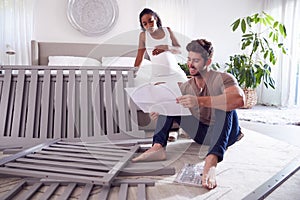 Couple With Pregnant Woman Looking At Instructions For Self Assembly Baby Cot
