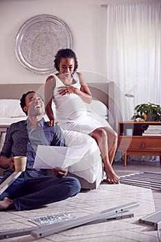 Couple With Pregnant Woman Looking At Instructions For Self Assembly Baby Cot