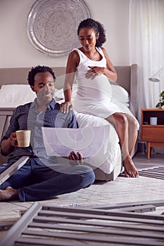 Couple With Pregnant Woman Looking At Instructions For Self Assembly Baby Cot