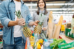 Couple puts pineapple into the cart in supermarket