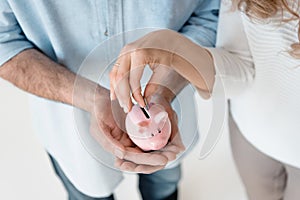 Couple putting coin into small piggy bank