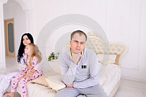 Couple quarrel and child upset, sitting bed in white interior