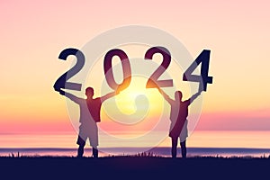 Couple raise hand up and holding number 2024 on sunset sky at tropical beach abstract background. Happy new year and holiday