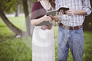 Couple reading the bible in a garden under sunlight with a blurry background